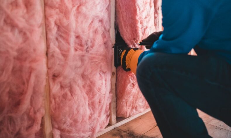 Crop unrecognizable worker in gloves sitting on haunches and insulating with pink stone wool - Photo by Erik Mclean on Pexels
