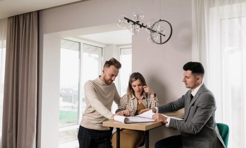 A couple consults with a real estate agent in a modern indoor setting, reviewing property documents. - Photo by Alena Darmel on Pexels